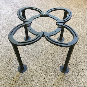May include: A black metal table with a unique design made from four horseshoes. The table has four legs and is sitting on a beige carpet.