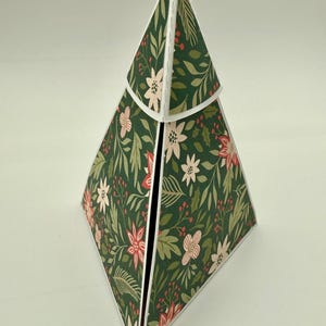 May include: A decorative, geometric paper box in a Christmas tree shape. The box is covered in a dark green floral pattern with red and pink flowers and white accents. The box is open at the top.