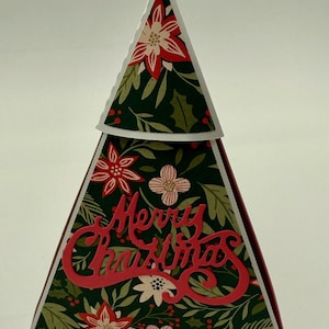 May include: A Christmas tree-shaped card with a dark green floral pattern featuring red poinsettias and white flowers. The words "Merry Christmas" are cut out in red script across the front. The card is a festive holiday decoration.