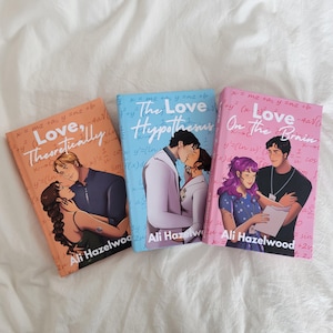 Puede incluir: Tres libros de bolsillo con ilustraciones románticas. Los títulos de los libros son "Love, Theoretically", "The Love Hypothesis" y "Love on the Brain" de Ali Hazelwood. Las portadas presentan parejas en varias poses románticas, sobre fondos coloridos.