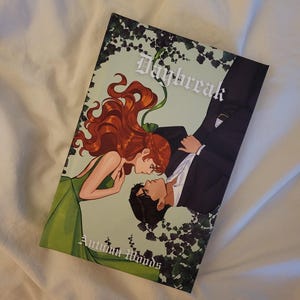 May include: A rectangular book cover titled Daybreak by Autumn Woods, featuring an illustration of a person with long red hair in a green dress facing a person in a black suit, surrounded by dark green ivy leaves against a pale green background.