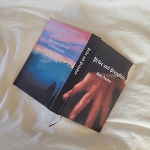 May include: A copy of "Pride and Prejudice" by Jane Austen. The cover shows a hand illustration and the title in white. The other side of the book has a quote and a painting of a person in a landscape with a sunset.