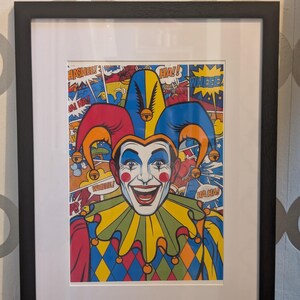 May include: Framed pop art print of a smiling jester with a colorful costume. The jester has a white face, red lips, and blue eye makeup. Speech bubbles with words like "HA!" and "WHEEE!" are in the background.