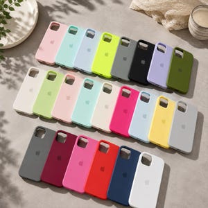 May include: A collection of twenty-three silicone phone cases arranged in three rows, featuring a variety of solid colors including pink, mint, blue, neon yellow, gray, black, lavender, olive, white, lime, peach, cream, magenta, and red.