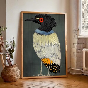 May include: A framed art print featuring a stylized bird illustration. The bird has a black head, a red eye, and a yellow and white body with orange and black accents. The artwork is set against a dark green background.