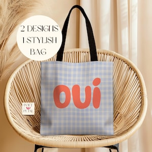 May include: A tote bag with a light blue gingham pattern and the word "OUI" in coral letters. The bag has black handles and is displayed on a wicker chair. Text on the bag reads "2 Designs 1 Stylish Bag."