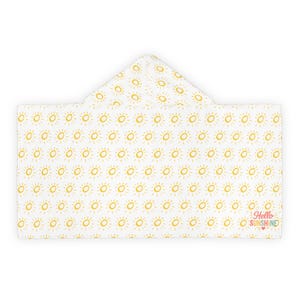 Op de afbeelding: Witte badhanddoek met capuchon met een herhalend patroon van gele zonnen. De handdoek heeft de tekst "Hello Sunshine" in roze en rood. De handdoek is gemaakt van een zacht materiaal.