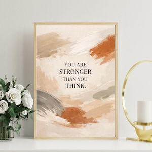 Puede incluir: Impresión artística enmarcada con pinceladas abstractas en tonos beige, marrón y naranja. El texto "YOU ARE STRONGER THAN YOU THINK" está centrado en la obra de arte. La impresión se muestra sobre una superficie blanca.