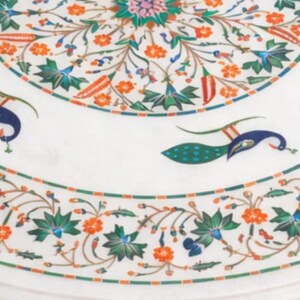 K&ouml;nnte beinhalten: Runder wei&szlig;er Marmortisch mit aufwendigem Blumen- und Pfauenfedern-Inlay. Das Design enth&auml;lt orange, gr&uuml;ne, blaue und rosa Akzente. Der Tisch hat einen dekorativen Rand und misst etwa 100 cm im Durchmesser.