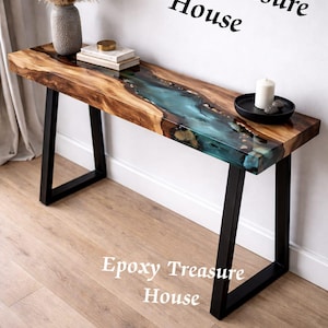 May include: A wooden console table with a blue epoxy river design. The table has a natural wood grain finish and black metal legs. The text "Epoxy Treasure House" is displayed on the image. A vase with dried plants, books, and a candle are on the table.