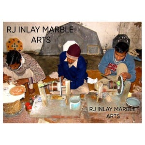 K&ouml;nnte beinhalten: Drei Kunsthandwerker arbeiten an Marmor-Intarsienkunst. Jede Person sitzt und verwendet eine kleine Schleifscheibe, um die Marmorst&uuml;cke zu formen und zu verfeinern. Der Text "RJ Inlay Marble Arts" ist im Bild zu sehen.