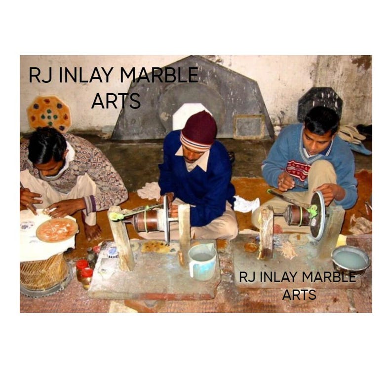 K&ouml;nnte beinhalten: Drei Kunsthandwerker arbeiten an Marmor-Intarsienkunst. Jede Person sitzt und verwendet eine kleine Schleifscheibe, um die Marmorst&uuml;cke zu formen und zu verfeinern. Der Text "RJ Inlay Marble Arts" ist im Bild zu sehen.