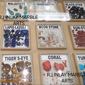 K&ouml;nnte beinhalten: Eine Ausstellung verschiedener Edelsteine, darunter Malachit, Lapislazuli und Koralle, jeweils in einzelnen Vitrinen beschriftet. Der Text "RJ INLAY MARBLE ARTS" ist sichtbar. Das Bild zeigt eine Vielfalt an Farben und Texturen.