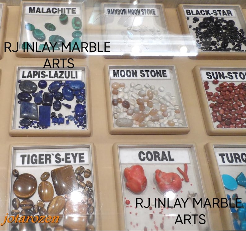 K&ouml;nnte beinhalten: Eine Ausstellung verschiedener Edelsteine, darunter Malachit, Lapislazuli und Koralle, jeweils in einzelnen Vitrinen beschriftet. Der Text "RJ INLAY MARBLE ARTS" ist sichtbar. Das Bild zeigt eine Vielfalt an Farben und Texturen.