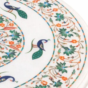 K&ouml;nnte beinhalten: Nahaufnahme einer wei&szlig;en Marmortischplatte mit aufwendigen Blumen- und Pfauendesigns. Der Rand weist ein blaues, orangefarbenes und gr&uuml;nes Muster auf. Der Pfau ist in Blau, Gr&uuml;n und Wei&szlig; dargestellt.