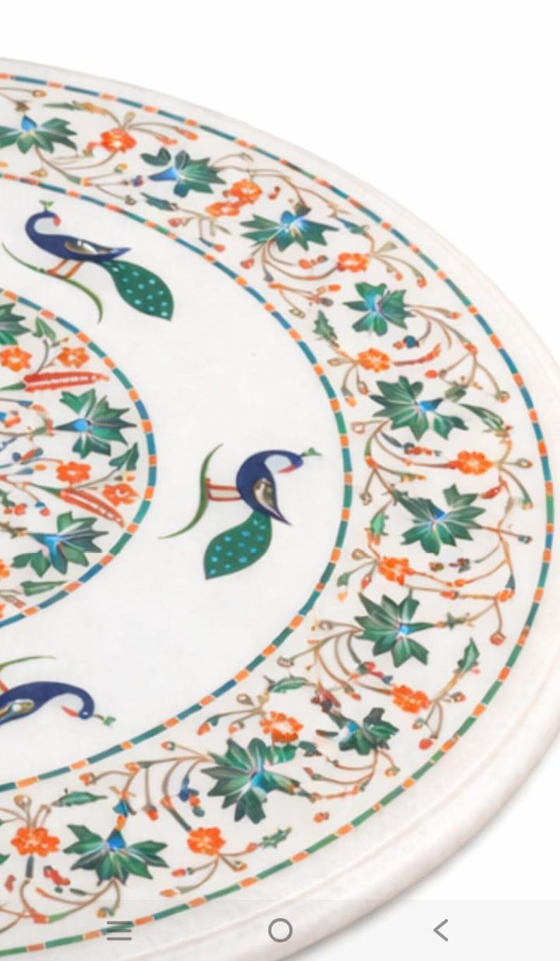 K&ouml;nnte beinhalten: Nahaufnahme einer wei&szlig;en Marmortischplatte mit aufwendigen Blumen- und Pfauendesigns. Der Rand weist ein blaues, orangefarbenes und gr&uuml;nes Muster auf. Der Pfau ist in Blau, Gr&uuml;n und Wei&szlig; dargestellt.