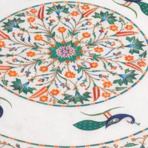 K&ouml;nnte beinhalten: Wei&szlig;er Marmortisch mit aufwendigem Blumen- und Pfaueneinlegearbeiten. Der runde Tisch hat ein zentrales Blumenmedaillon und einen Rand mit Pfauen- und Blumenmotiven in Orange, Gr&uuml;n und Blau. Durchmesser ca. 100 cm.