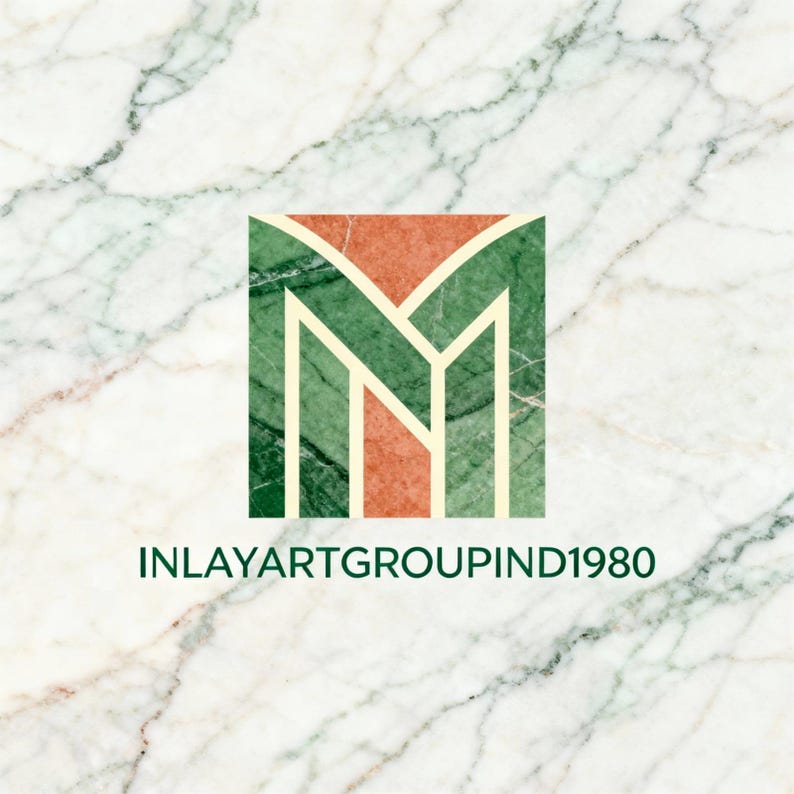K&ouml;nnte beinhalten: Ein quadratisches Logo mit einem stilisierten gr&uuml;nen und orangefarbenen "M" auf Marmorhintergrund. Der Text "INLAYARTGROUPIND1980" steht darunter. Der Marmor hat wei&szlig;e und graue Adern.