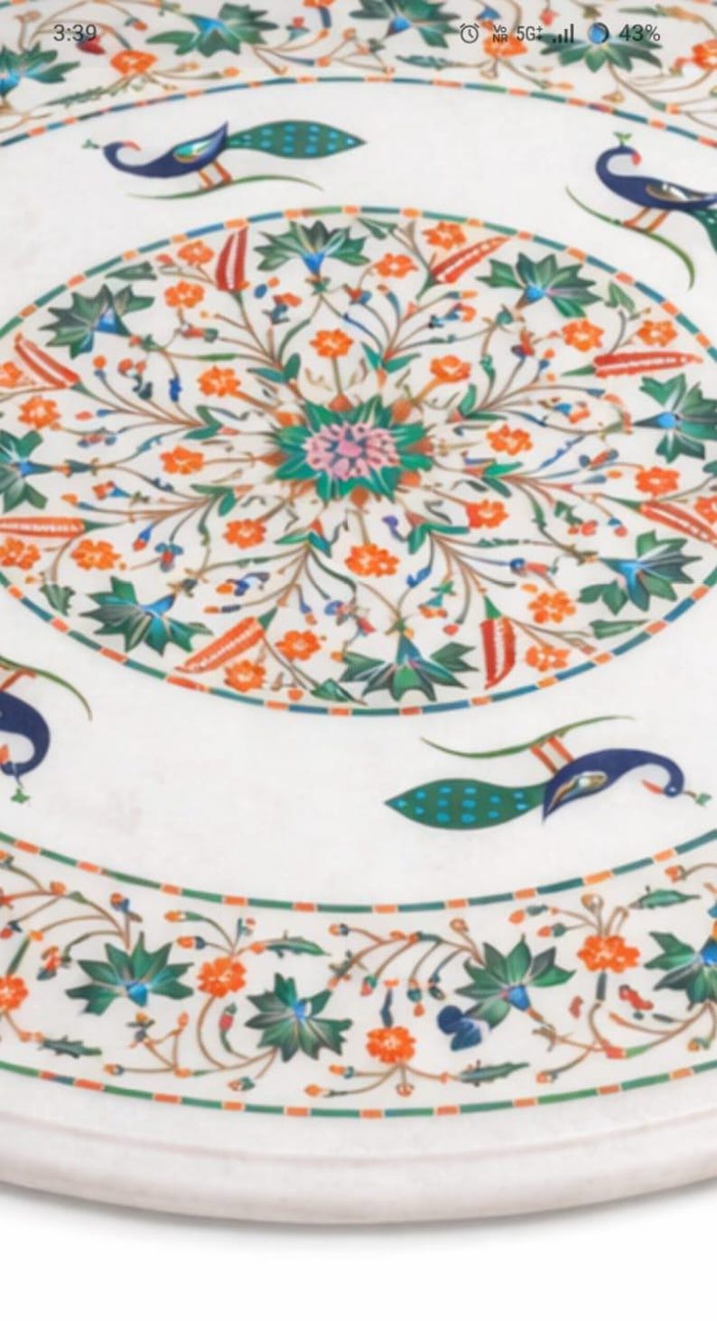 K&ouml;nnte beinhalten: Wei&szlig;er Marmor-Tischplatte mit aufwendigem Blumen- und Pfauendesign. Das Design weist orange, gr&uuml;ne, blaue und rosa Akzente auf. Die Tischplatte hat eine kreisf&ouml;rmige Form und dient wahrscheinlich dekorativen Zwecken.