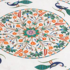 K&ouml;nnte beinhalten: Runde Tischplatte aus wei&szlig;em Marmor mit aufwendigem Blumen- und Pfauenmuster. Das Design weist orange, gr&uuml;ne, blaue und rote Akzente auf. Der Tisch hat eine kreisf&ouml;rmige Form.