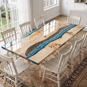 May include: A large, rectangular dining table with a light wood grain finish and a blue epoxy river design. The table is surrounded by white wooden chairs and sits on a patterned rug. The table's dimensions are approximately 100 inches long and 40 inches wide.