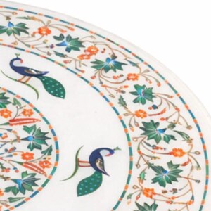K&ouml;nnte beinhalten: Wei&szlig;er Marmor-Tischplatte mit aufwendigem Pfau- und Blumen-Intarsien-Design. Das Design weist blaue, gr&uuml;ne und orangefarbene Akzente auf. Die Tischplatte hat eine runde Form.