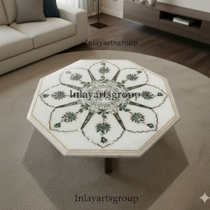 May include: Octagonal white marble coffee table with a floral inlay design in green and gold. The table has a single central leg and is set on a neutral rug. The table's surface features the text "Inlayartsgroup".