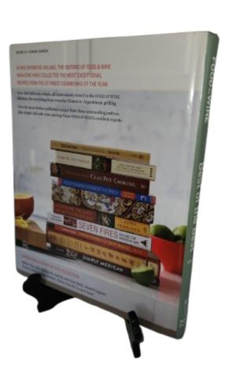 May include: A stack of cookbooks, including "Seven Fires" and "Simply Mexican", is displayed on a book stand. The cover of the book on the front says "Food & Wine Best of the Best". The books are on a white surface.