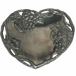 May include: A heart-shaped, silver-toned serving tray. The tray features a grape and vine design around the edges and on the surface. The tray has a smooth, reflective surface and is likely made of metal.
