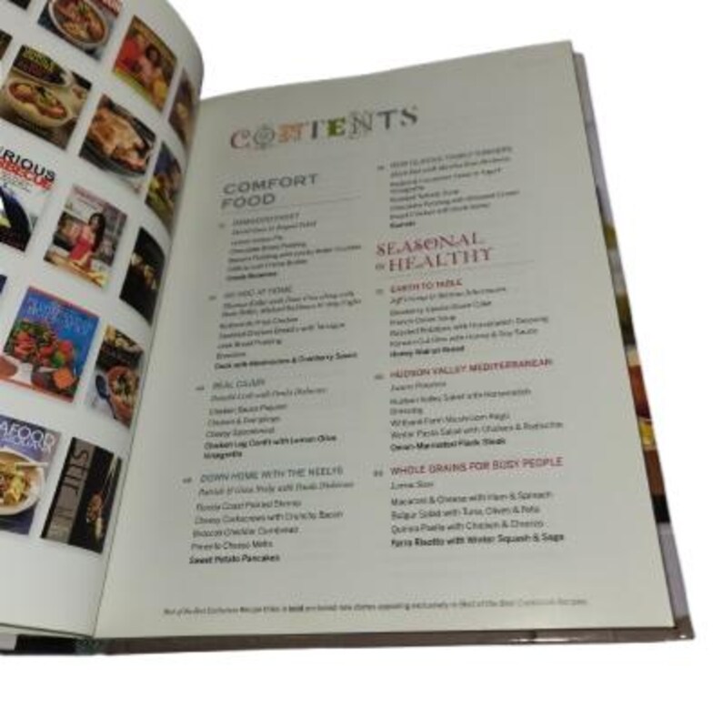 May include: Open cookbook with a table of contents. The left page displays colorful book covers with food images. The right page lists categories like "Comfort Food" and "Seasonal & Healthy" with various recipes.