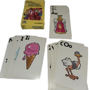 May include: A set of alphabet flash cards with illustrations and uppercase and lowercase letters. The cards feature images like an angel, ice cream, and an ostrich. The box reads "Golden Step Ahead Alphabet Flash Cards" and indicates there are 54 cards.