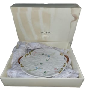 May include: A white serving platter with a floral design, presented in a box. The platter has a textured surface and brown handles. The box is off-white with the word "BELLEEK" printed on it.