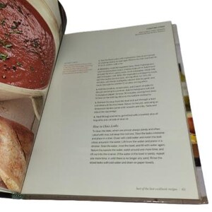 May include: Open cookbook with a recipe for a tomato-based dish. The left page shows a close-up of the prepared food in a bowl. The right page has text with instructions. The book is open to the "Test of the best cookbook recipes" section.