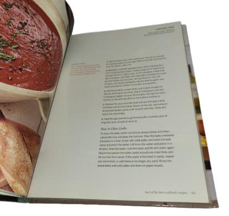 May include: Open cookbook with a recipe for a tomato-based dish. The left page shows a close-up of the prepared food in a bowl. The right page has text with instructions. The book is open to the "Test of the best cookbook recipes" section.