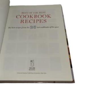May include: Open cookbook titled "Best of the Best Cookbook Recipes." The cover features red text on a white background. The book is open to a page with the title and a subtitle, "The best recipes from the 25 best cookbooks of the year."