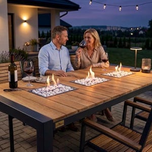 Puede incluir: Una mesa de comedor rectangular para exteriores con tablero de listones de madera natural y marco de metal oscuro, que cuenta con tres fogatas rectangulares integradas llenas de piedras blancas y llamas activas en un patio pavimentado.