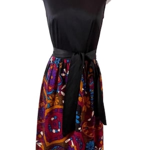May include: A sleeveless black dress with a colorful paisley print skirt. The dress features a black bodice, a black waist tie, and a vibrant skirt with red, purple, blue, and orange floral patterns. The neckline has a colorful patterned trim.