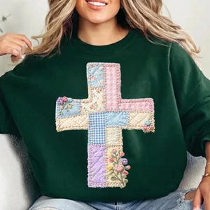 May include: A dark green sweatshirt featuring a patchwork cross design. The cross is made of various pastel fabrics, including gingham and floral patterns, with embroidered details. The sweatshirt has a crew neck and long sleeves.