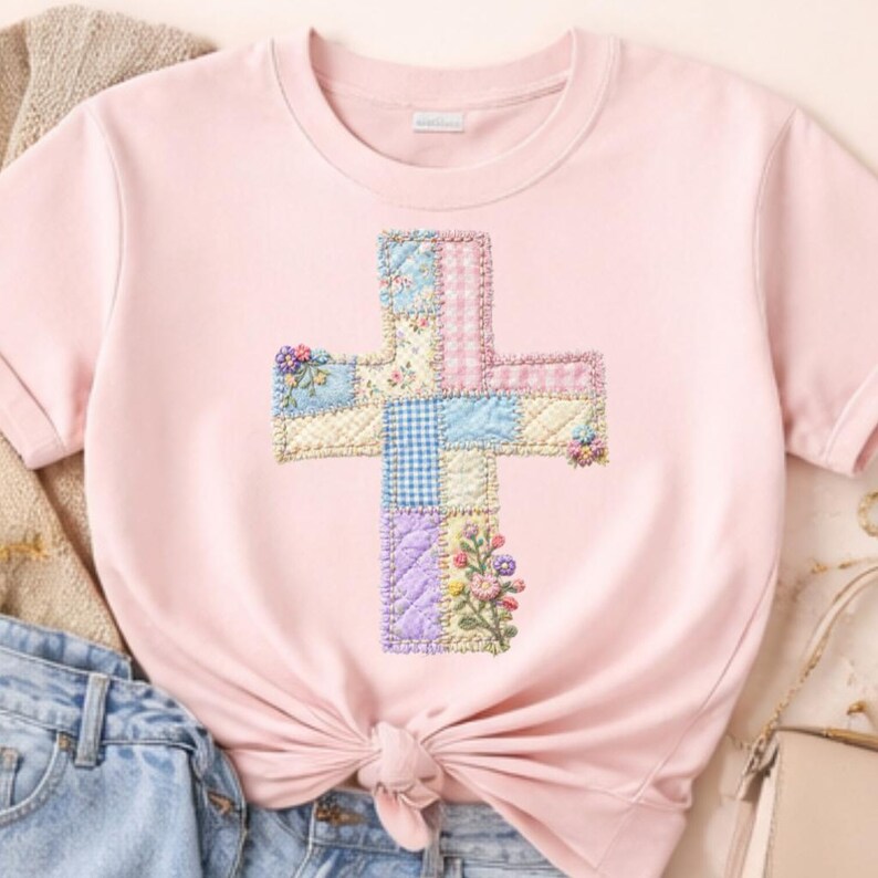 May include: A light pink t-shirt featuring a cross design. The cross is made of patchwork squares in pastel colors, including blue, pink, and yellow, with floral and gingham patterns. The shirt has short sleeves and a tied knot at the waist.