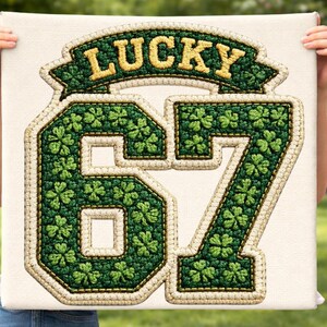 May include: A canvas featuring a green and gold embroidered design. The design includes the word "LUCKY" above the number "67", with shamrock details. The canvas has a cream-colored background.