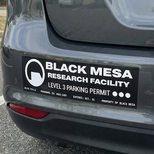 Puede incluir: Adhesivo de permiso de estacionamiento de nivel 3 de Black Mesa Research Facility en un coche gris. El adhesivo rectangular tiene texto blanco y un logotipo sobre un fondo negro. El texto incluye el nombre de la instalación y la fecha de caducidad.