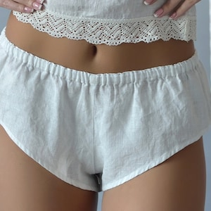 May include: White linen shorts with a gathered elastic waistband. The shorts are made of a lightweight, breathable fabric and have a relaxed fit.