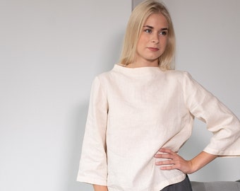 May include: A woman wearing a cream-colored linen top with three-quarter sleeves and a gray maxi skirt with a ruffled hem. She is wearing brown leather boots. The outfit is casual and elegant.