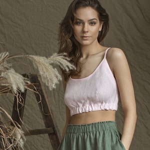 May include: A woman wearing a pink linen crop top with a gathered elastic waistband and green linen pants with a drawstring waist.