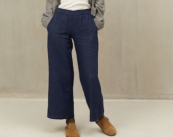 May include: A woman wearing a gray linen jacket, a white t-shirt, dark blue linen pants, and brown leather shoes.