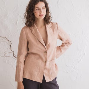 Può includere: Un blazer color marrone chiaro a maniche lunghe, con revers a dente e due bottoni frontali. Il capo presenta due ampie tasche applicate sulla parte inferiore ed è abbinato a pantaloni di colore grigio antracite scuro.
