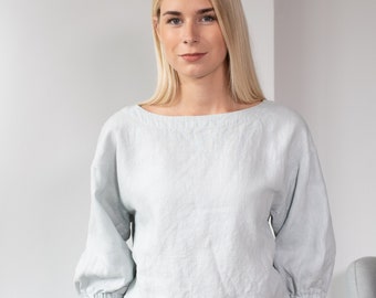 May include: A light blue linen blouse with a relaxed fit and 3/4 sleeves. The blouse has a boat neck and a slightly gathered waist.