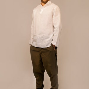May include: A white linen shirt with a mandarin collar and long sleeves. The shirt is tucked into brown pants and the person is wearing gray sneakers.