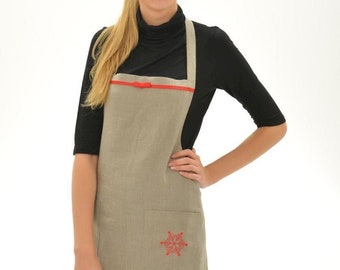 May include: A beige linen apron with a red ribbon and a red snowflake design. The apron has a large pocket on the front.