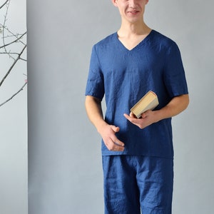Pode incluir: Um homem vestindo uma camisa de linho azul de manga curta e shorts combinando. Ele est&aacute; segurando um livro na m&atilde;o direita.